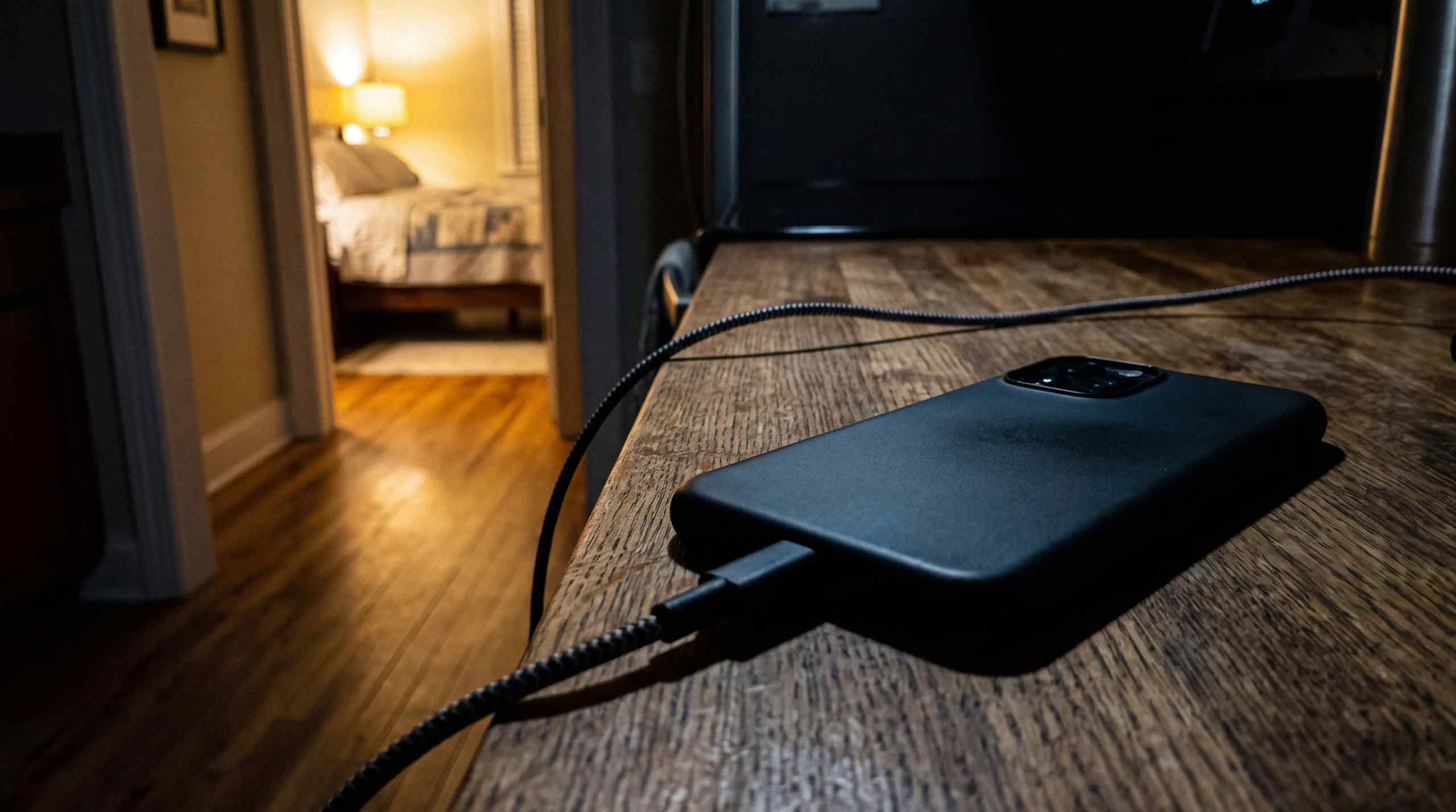 A phone charging in a separate room away from the bedroom.